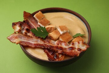 Delicious lentil soup with bacon and parsley in bowl on green table, closeup