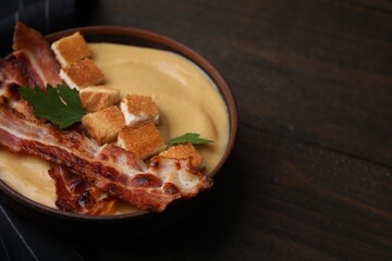 Delicious lentil soup with bacon and parsley in bowl on wooden table, closeup. Space for text