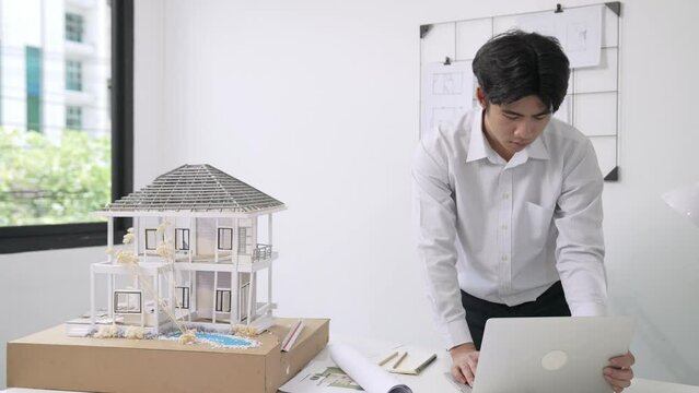 Close up of professional male architect engineer measure house model and using laptop analysis data at meeting table with house model and map . scatter around. Focus on hand. Immaculate.