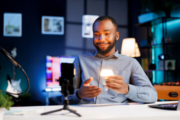 Online star doing technology video vlog, showcasing dimmable smart light bulb to viewers. Friendly...