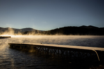 A foggy and steamy lake (Lake Dillon) on a cold winter morning at sunrise in the Rocky Mountains (Summit County, Colorado, USA) with a dock in the foreground