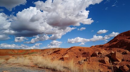 A striking contrast between the deep red bauxite ore and the bright white clouds in the sky above.