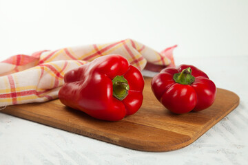 Cutting board with several whole red bell pepper and red kitchen towel on white wooden background. .
