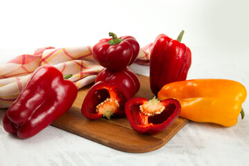 Cutting board with several whole and halves of red and yellow bell pepper and red kitchen towel on white wooden background. .