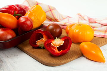 Cutting board with assort of different tomatoes and bell pepper on white wooden background..