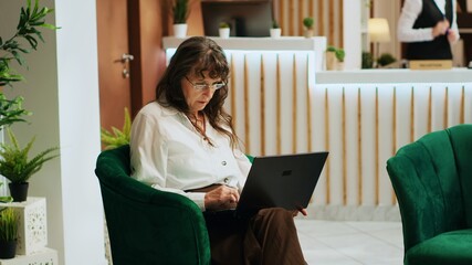 Senior tourist using laptop in lounge area, navigating internet to look at visiting places on...