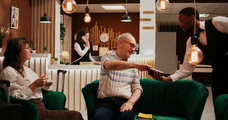 Retired couple paying for coffee cup from hotel bar, taking out credit card for pos terminal...