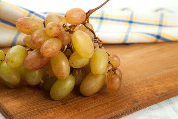 Cutting board with bunch of organic pink grapes on white wooden background..