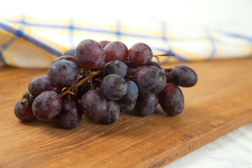 Cutting board with bunch of organic black grapes on white wooden background..