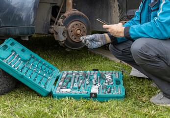 A mechanic is changing a car tire on the roadside, using a socket set and smartphone for guidance,...