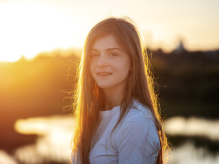 Sunny portrait of a happy girl with long hair in a white T-shirt. In the sunset