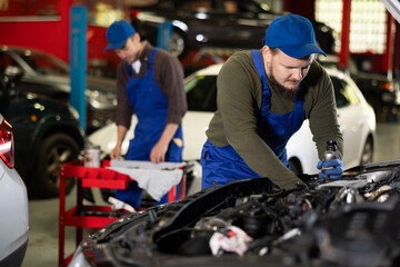 Qualified male worker of auto service center wearing blue working-clothes engaged in mending of...
