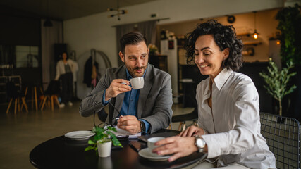 Two colleagues man and woman on break at cafe drink coffee and talk