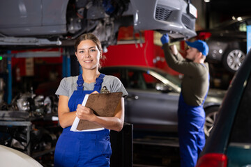Female car service worker keeps records of work performed by auto mechanics in a car service station - makes notes on paper