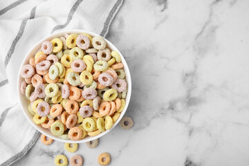 Tasty cereal rings in bowl on white marble table, top view. Space for text