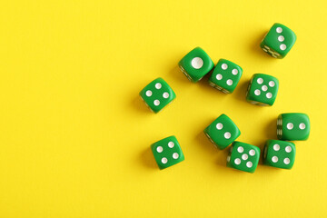 Many green game dices on yellow background, flat lay. Space for text