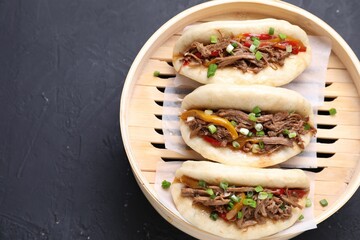 Delicious gua bao in bamboo steamer on black table, top view. Space for text