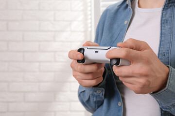 Man using wireless game controller indoors, closeup. Space for text
