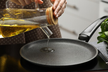 Vegetable fats. Woman pouring cooking oil into frying pan on stove in kitchen, closeup