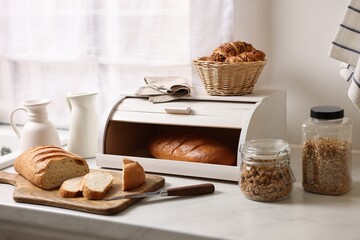 Wooden bread basket with freshly baked loaves on white marble table in kitchen