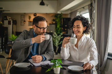 Two colleagues man and woman on break at cafe drink coffee and talk