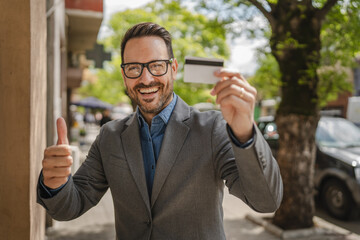 Portrait of adult caucasian man stand and hold credit card on street