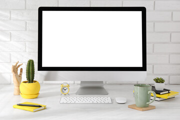 Office workplace with computer, stationery, cup and houseplants on light table near white brick wall