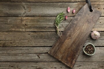 Cutting board, garlic, pepper and rosemary on wooden table, flat lay. Space for text