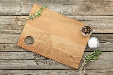 Cutting board, rosemary, salt and pepper on wooden table, flat lay. Space for text