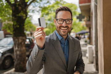 Portrait of adult caucasian man stand and hold credit card on street