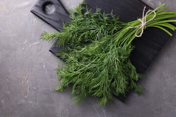 Board with bunch of fresh dill on grey textured table, top view. Space for text