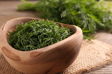 Fresh cut dill in bowl on wooden table, closeup