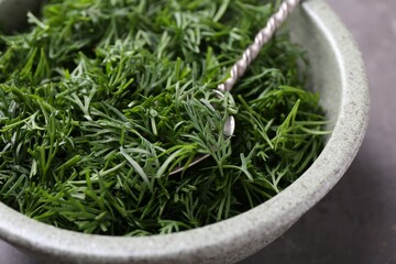 Fresh cut dill and spoon in bowl on table, closeup