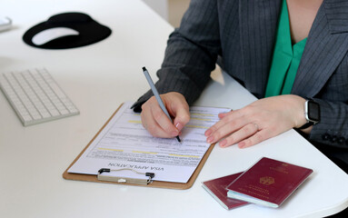 Top view of a woman filling out visa application documents with a German passport on a office table