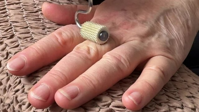 An unknown elderly woman sitting in an armchair makes herself a hand massage with her hand with a massager in the form of a needle-shaped silver roller. Health maintenance and Promotion Program