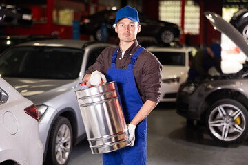 Young guy mechanic in uniform posing gasoline in container in car service station