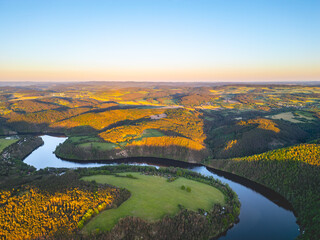 Aerial view of the Solenice Horseshoe Bend on the Vltava River in Czechia, showcasing the winding river surrounded by lush greenery and a small village during a picturesque sunset. - Powered by Adobe