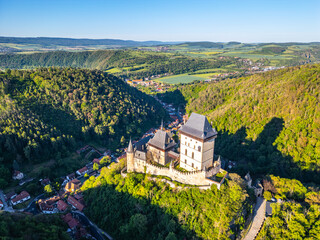 Aerial perspective of Karlstejn Castle nestled in a forested landscape with surrounding lush...