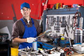 Young guy mechanic in uniform posing with wheel wrench in car service station