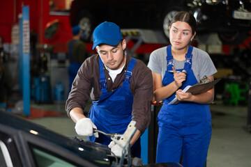 Woman with documents looks at guy mechanic fixing car in car service station
