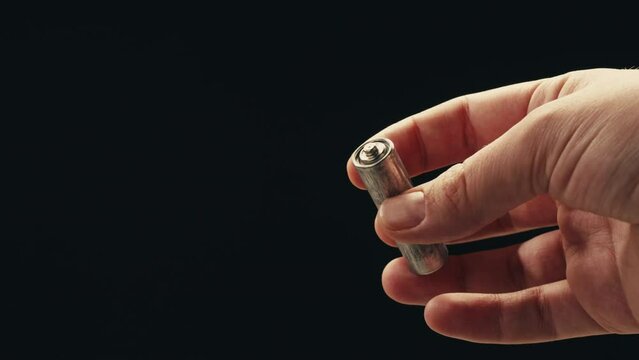 Silver batteries AA and AAA in hands on black background close-up. Double-A battery is a standard size single cell cylindrical dry battery. Batteries are common in portable electronic devices. An AA