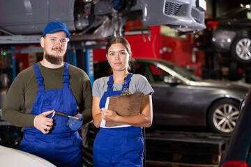 Positive car mechanic standing in auto service shop together with female worker ready to take note
