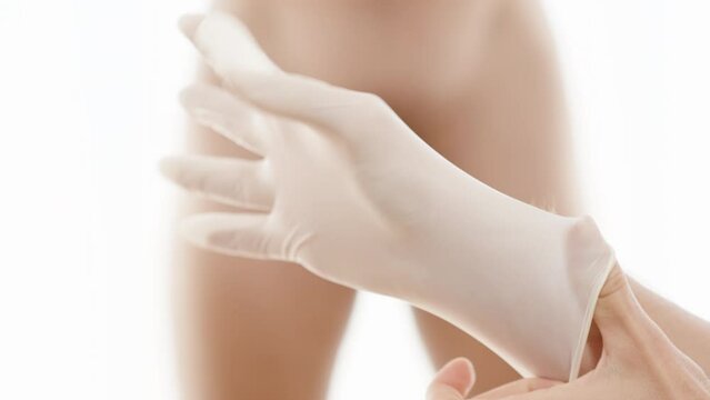 A woman's hand puts on a glove, a doctor's examination. A naked man in the background covers himself with his hands.