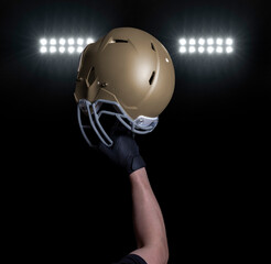 Football player holding his helmet up under stadium lights at night