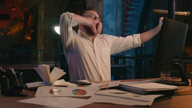 Caucasian man business guy businessman male workaholic in dark night office overworked overtime tired exhausted yawning low energy late time need sleep deadline working computer yawn health insomnia