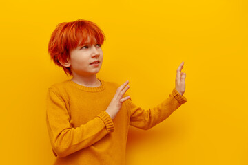 dissatisfied red-haired teenage boy avoids and rejects with his hands on a yellow isolated...