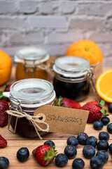 Glass jars with homemade jam decorated with handmade brown cardboard labels attached with string. In the foreground, a jar of homemade strawberry jam, vertical image for social media or posters.