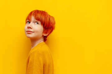 red-haired boy child looking back on yellow isolated background, teenager with orange hairstyle asks not to speak and be quieter