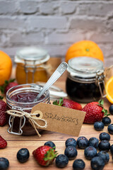 Glass jars with homemade jam decorated with handmade brown cardboard labels attached with string. In the foreground, a jar of homemade strawberry jam, vertical image for social media or posters.