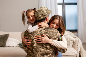 Ukrainian military man in camouflage uniform hugs his family at home and smiles, a happy soldier of...